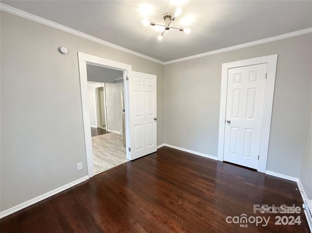 unfurnished bedroom featuring a notable chandelier, crown molding, and dark hardwood / wood-style flooring