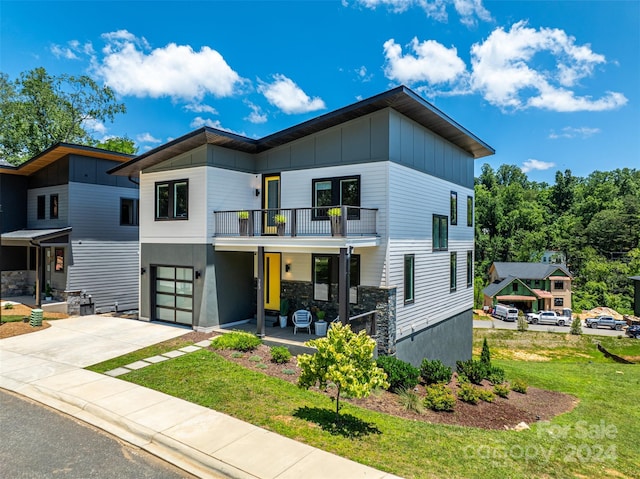 contemporary home with a front yard, a balcony, a porch, concrete driveway, and board and batten siding