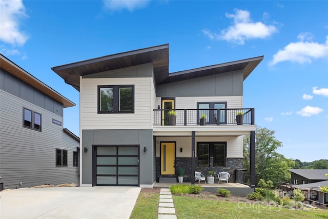 contemporary house with a balcony, an attached garage, covered porch, concrete driveway, and board and batten siding