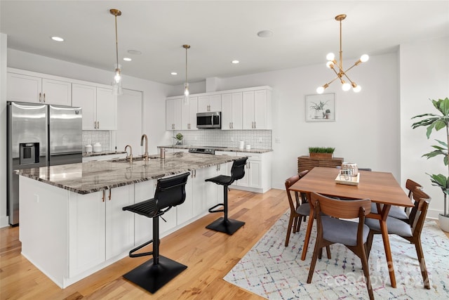 kitchen with stone counters, light wood-style flooring, white cabinets, stainless steel appliances, and a sink