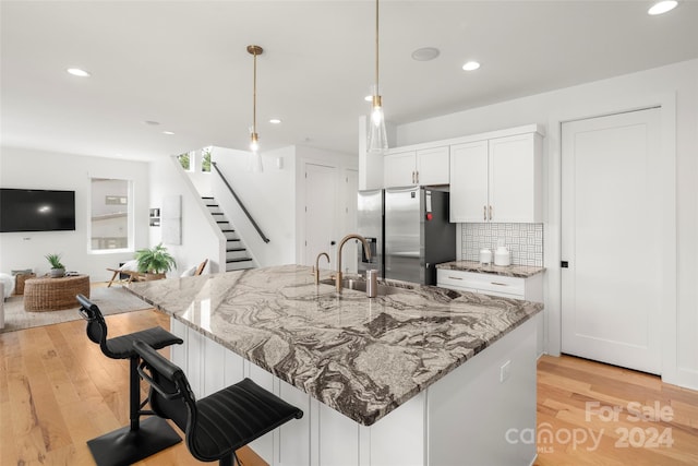 kitchen featuring a sink, tasteful backsplash, a breakfast bar area, stainless steel fridge with ice dispenser, and light wood finished floors