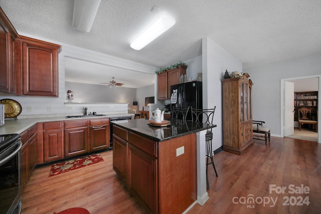 kitchen with black refrigerator, a breakfast bar, ceiling fan, dark stone countertops, and a kitchen island