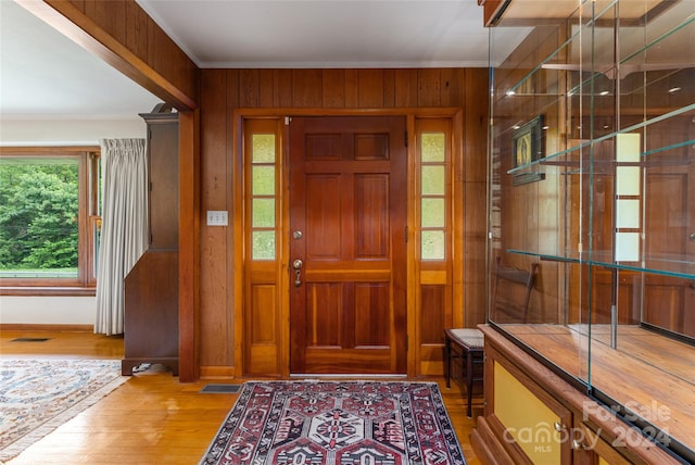 foyer with ornamental molding, wooden walls, and light wood-type flooring