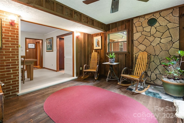 living area featuring wooden walls, a textured ceiling, ceiling fan, and wood-type flooring