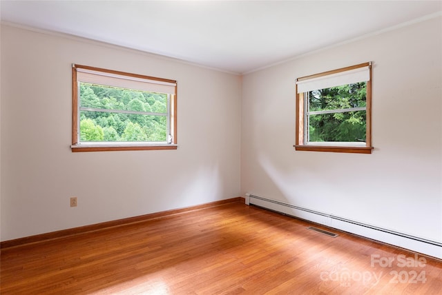 spare room with a baseboard heating unit, a wealth of natural light, and hardwood / wood-style flooring