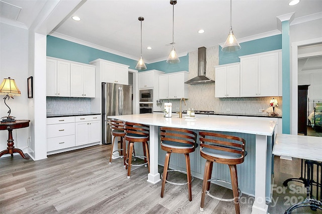 kitchen with hanging light fixtures, white cabinetry, stainless steel appliances, and wall chimney exhaust hood