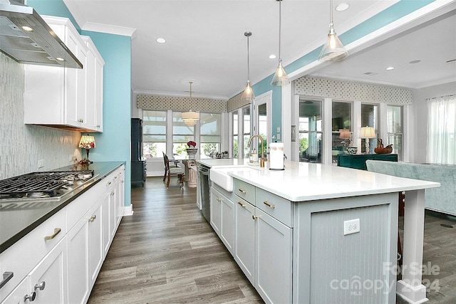 kitchen featuring appliances with stainless steel finishes, a large island with sink, wall chimney exhaust hood, white cabinets, and hanging light fixtures