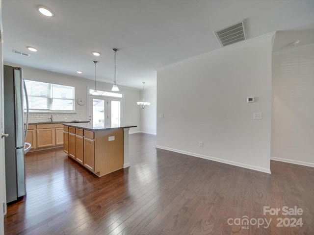 kitchen featuring a center island, dark hardwood / wood-style flooring, decorative backsplash, crown molding, and stainless steel refrigerator