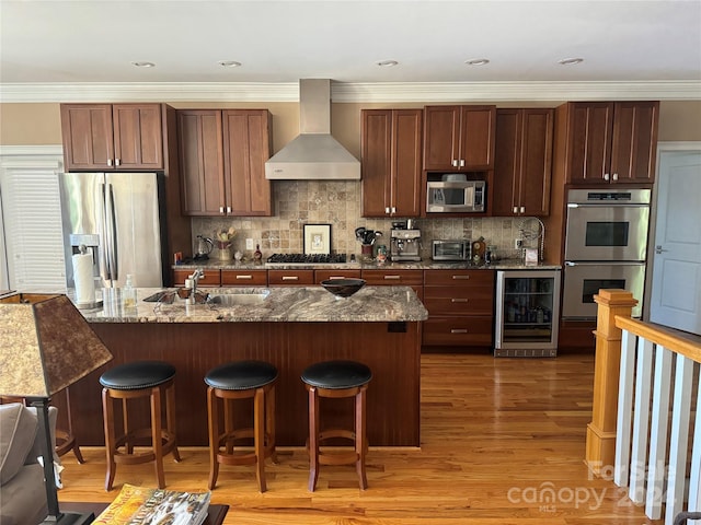 kitchen with sink, wall chimney range hood, wine cooler, dark stone counters, and appliances with stainless steel finishes