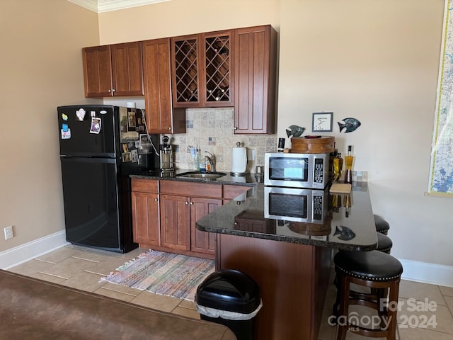 kitchen with sink, black fridge, dark stone countertops, light tile patterned floors, and ornamental molding