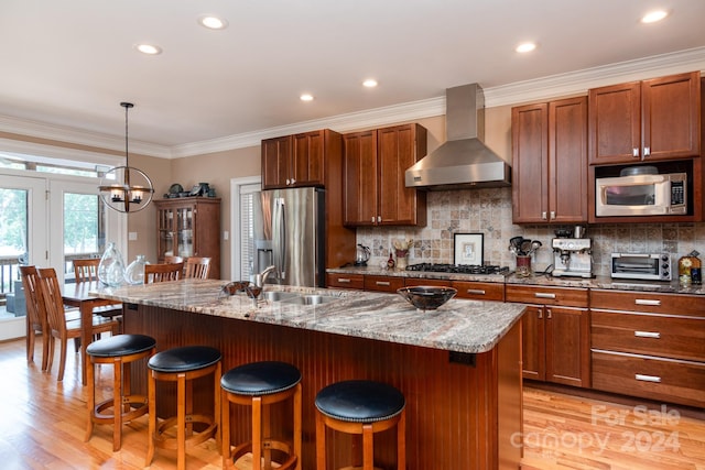 kitchen featuring an inviting chandelier, an island with sink, wall chimney range hood, and appliances with stainless steel finishes