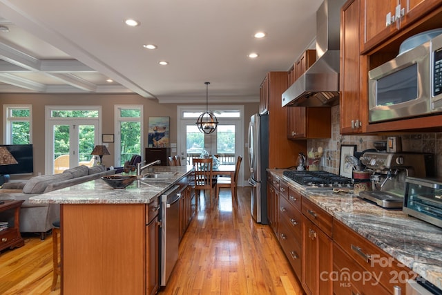 kitchen with a kitchen breakfast bar, light stone counters, stainless steel appliances, wall chimney range hood, and a center island with sink