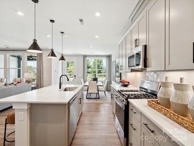 kitchen with tasteful backsplash, pendant lighting, sink, appliances with stainless steel finishes, and an island with sink