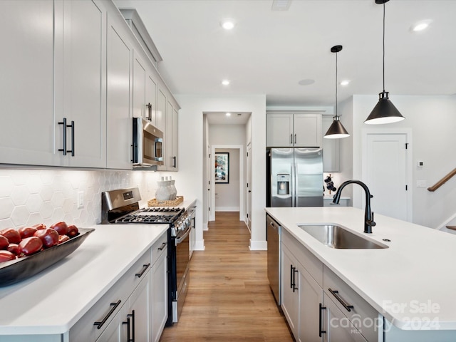 kitchen with stainless steel appliances, backsplash, a kitchen island with sink, pendant lighting, and sink