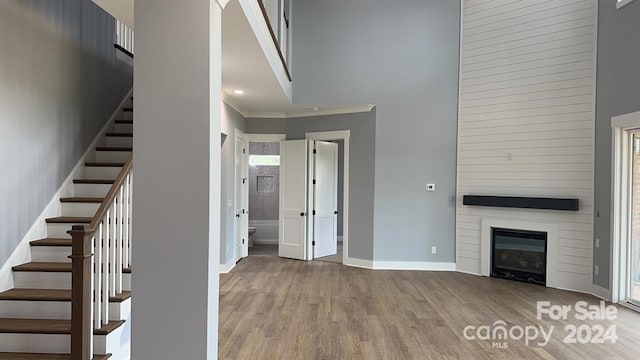 unfurnished living room featuring a towering ceiling, a fireplace, crown molding, and hardwood / wood-style floors