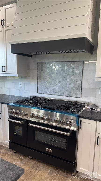 kitchen with premium range hood, double oven range, light hardwood / wood-style floors, decorative backsplash, and white cabinets