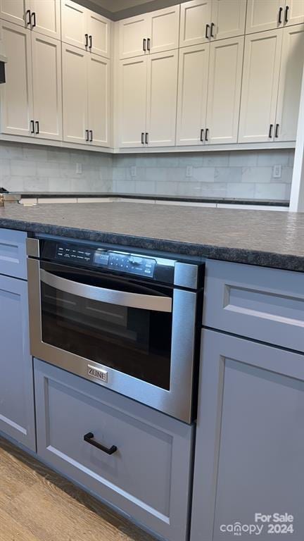 kitchen featuring tasteful backsplash, white cabinetry, light hardwood / wood-style floors, and oven