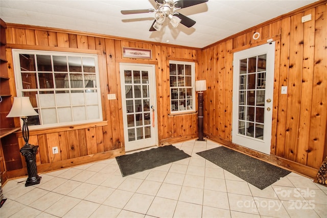 doorway to outside featuring ceiling fan, light tile patterned floors, crown molding, and wooden walls