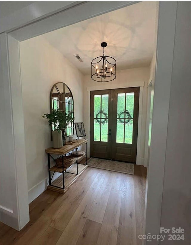 entryway featuring french doors, light wood-type flooring, and a notable chandelier