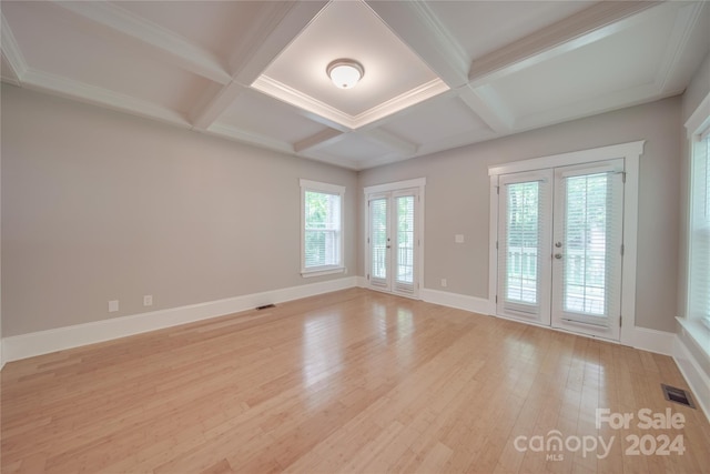 empty room featuring coffered ceiling, french doors, beamed ceiling, and light wood-type flooring