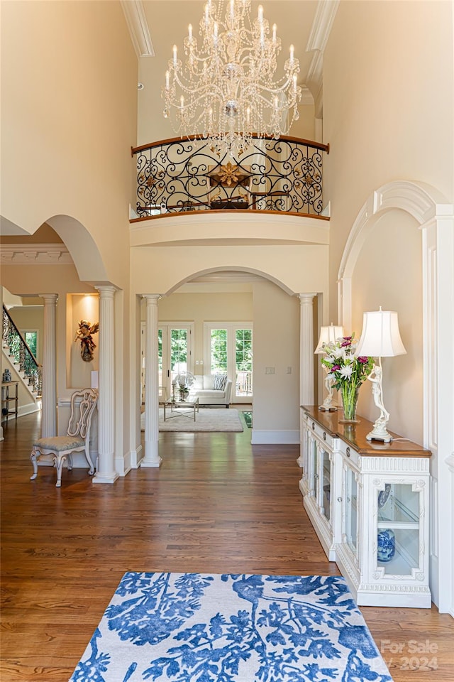 entryway featuring ornate columns, a notable chandelier, crown molding, hardwood / wood-style floors, and a towering ceiling