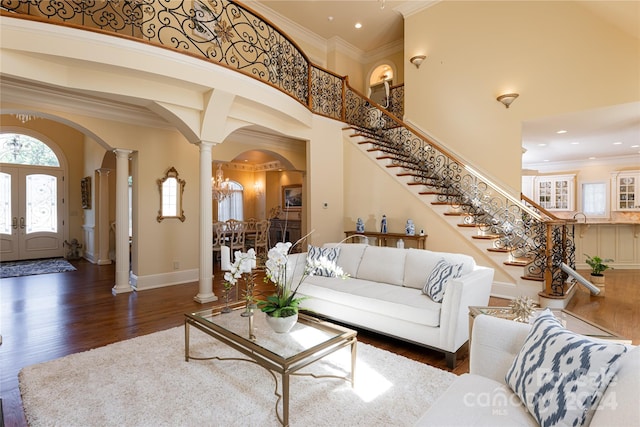 living room with dark wood-type flooring, french doors, ornate columns, ornamental molding, and a towering ceiling