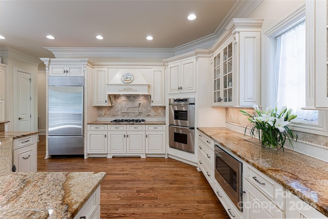 kitchen featuring white cabinetry, light stone counters, built in appliances, plenty of natural light, and custom range hood