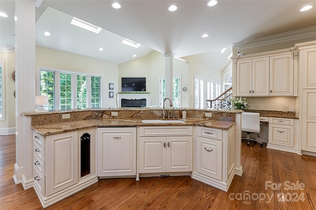 kitchen with dark wood-type flooring, sink, vaulted ceiling, light stone countertops, and a kitchen island