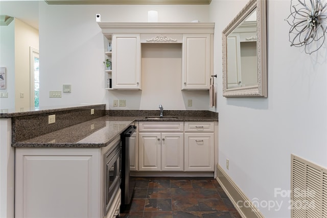 kitchen with white cabinets, kitchen peninsula, dark stone counters, and sink