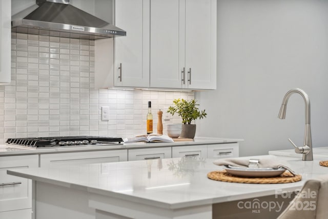 kitchen featuring light stone countertops, white cabinets, wall chimney exhaust hood, decorative backsplash, and stainless steel gas cooktop