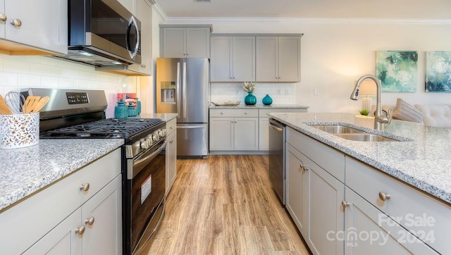 kitchen with appliances with stainless steel finishes, light stone counters, ornamental molding, and sink