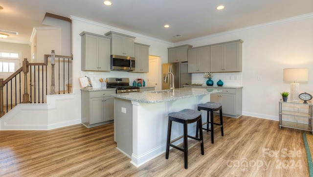 kitchen with gray cabinetry, stainless steel appliances, light hardwood / wood-style floors, a kitchen bar, and a center island with sink