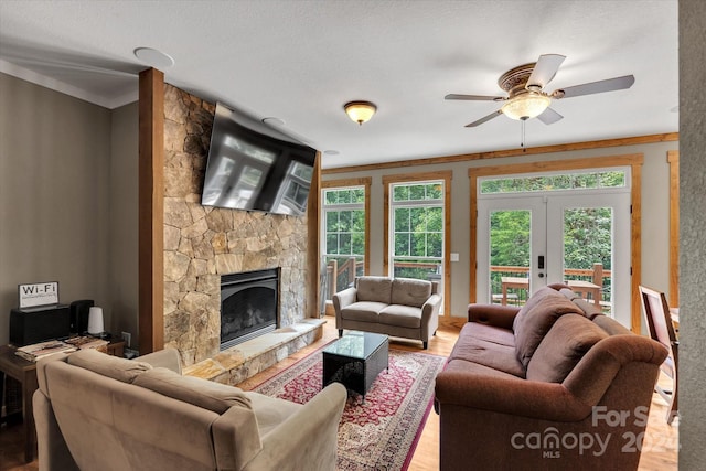 living room featuring french doors, crown molding, hardwood / wood-style flooring, and a stone fireplace