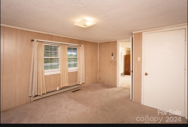 carpeted empty room with a textured ceiling and wooden walls