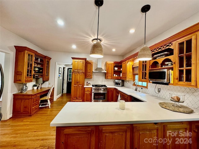 kitchen featuring kitchen peninsula, stainless steel appliances, hanging light fixtures, wall chimney range hood, and sink