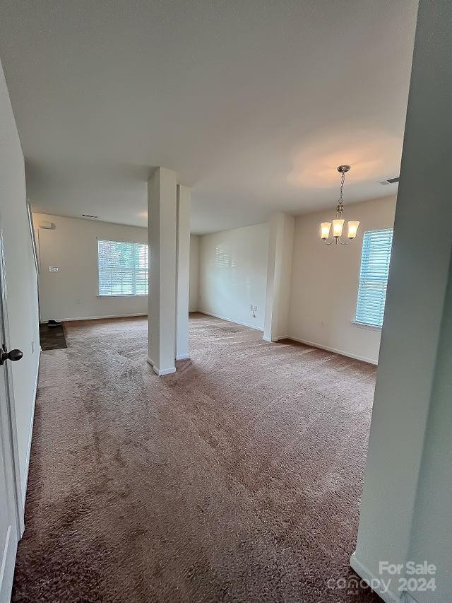 carpeted empty room featuring a notable chandelier