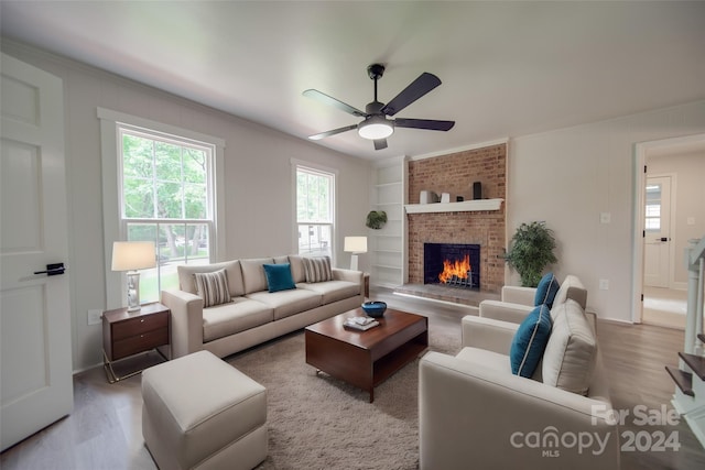 living room with a fireplace, ceiling fan, built in features, and light wood-type flooring