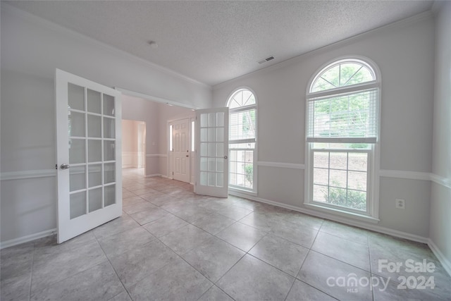 unfurnished room with light tile patterned floors, french doors, crown molding, and a textured ceiling