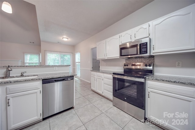 kitchen with light stone countertops, white cabinets, appliances with stainless steel finishes, sink, and light tile patterned floors