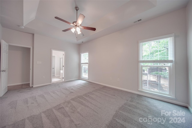 spare room with ceiling fan, a tray ceiling, and light carpet