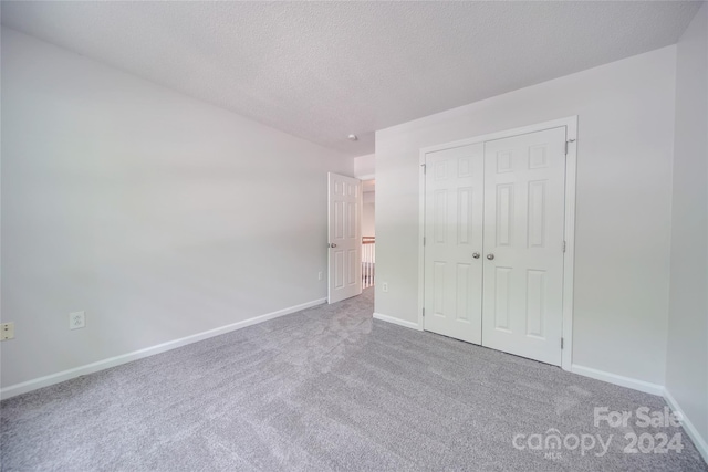 unfurnished bedroom featuring a textured ceiling, a closet, and light carpet