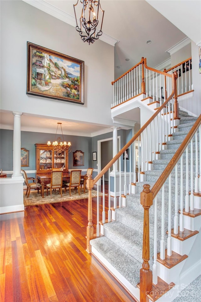 stairs with ornate columns, wood-type flooring, a notable chandelier, and ornamental molding