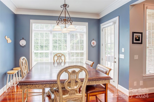 dining area with hardwood / wood-style flooring, plenty of natural light, ornamental molding, and an inviting chandelier