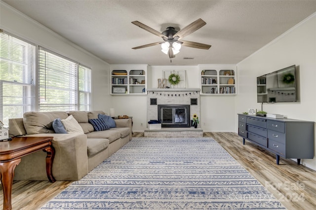 living room with a fireplace, light hardwood / wood-style flooring, a textured ceiling, and ornamental molding