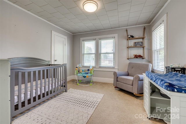 carpeted bedroom with a nursery area and ornamental molding