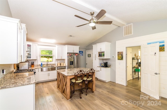 kitchen featuring light stone counters, stainless steel appliances, sink, white cabinets, and a center island