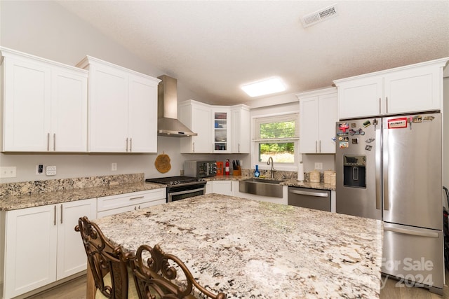 kitchen featuring light stone countertops, stainless steel appliances, sink, wall chimney range hood, and white cabinets