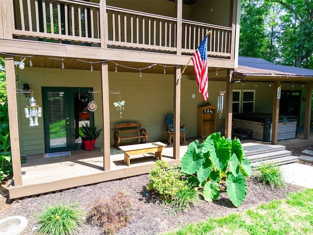 view of exterior entry featuring a balcony, a hot tub, and a patio area