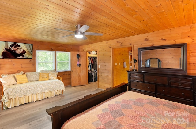 bedroom featuring ceiling fan, light hardwood / wood-style flooring, wood walls, a walk in closet, and a closet