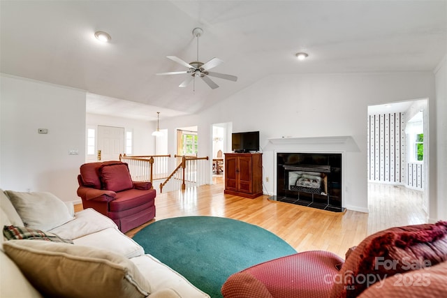 living room featuring a tile fireplace, vaulted ceiling, baseboards, light wood-style flooring, and ceiling fan